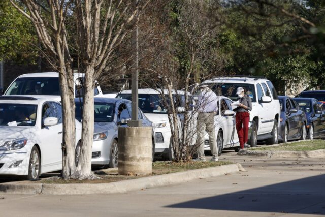 Dozens of people wait in their cars