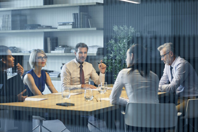 Coworkers communicating at desk seen through glass